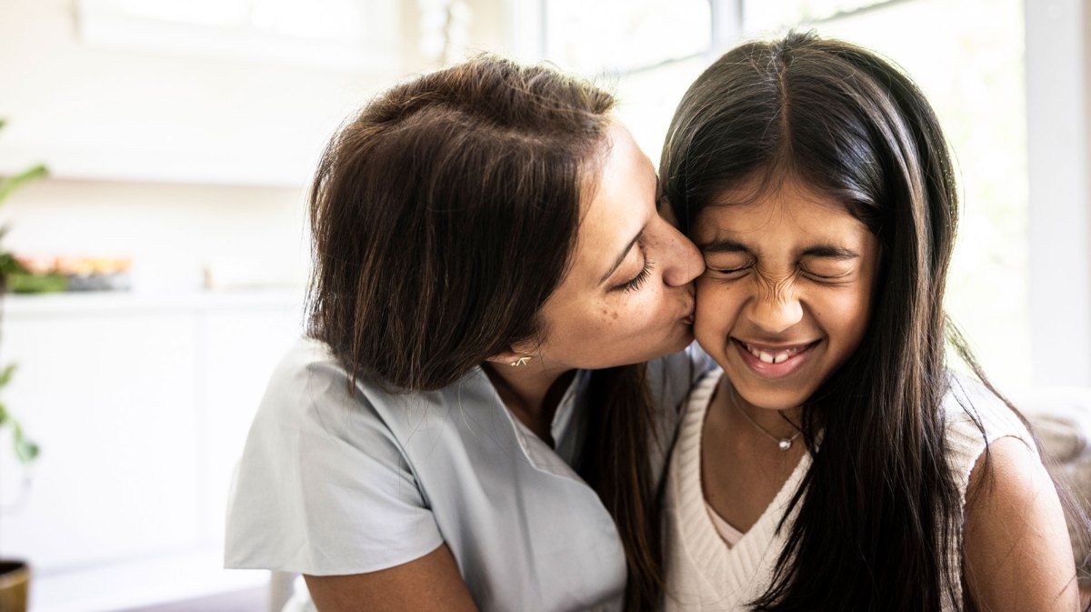 Mutter gibt ihrer Tochter einen Kuss auf die Wange, die verzieht witzig das Gesicht.