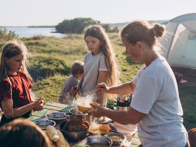 Familie auf einem Campingplatz kommt gerade zum Essen zusammen.