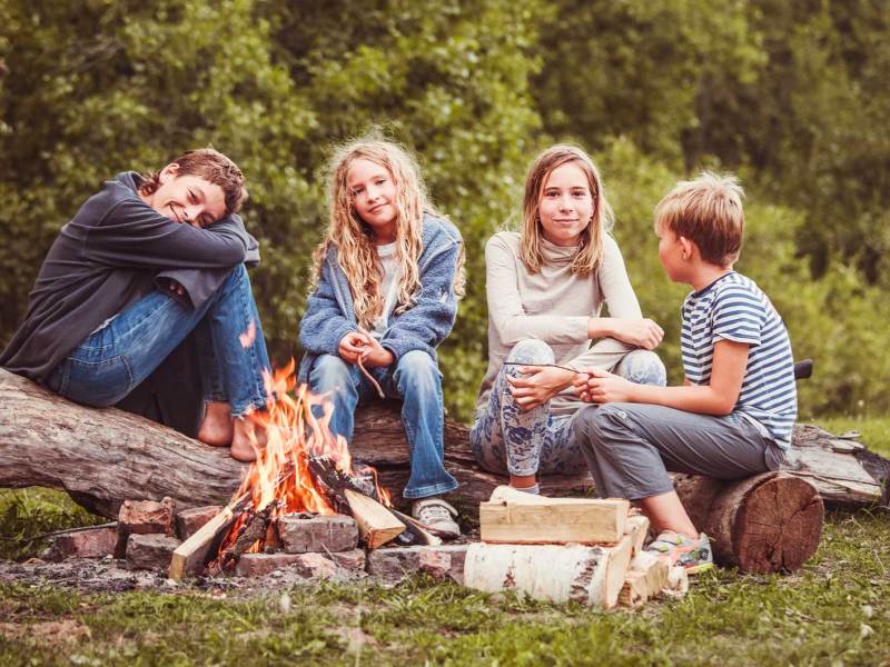 Vier Kinder zwischen 10 und 12 Jahren sitzen an einem Lagerfeuer.