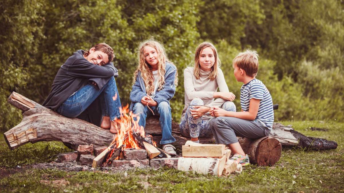 Vier Kinder zwischen 10 und 12 Jahren sitzen an einem Lagerfeuer.