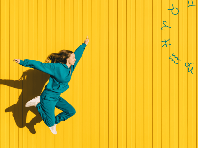 Frau in petrolfarbenen Jogginganzug springt vor gelber Wand