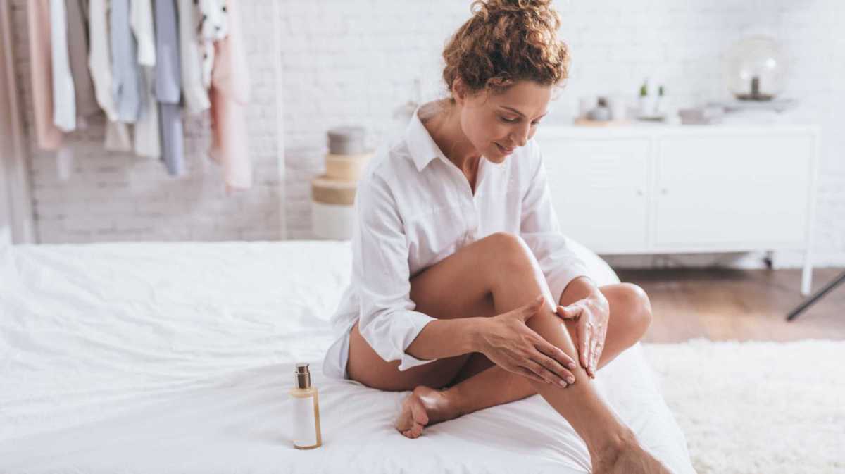 Frau cremt ihre Beine mit Lotion ein