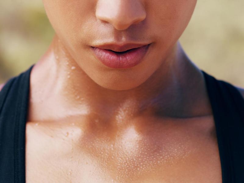 Frau mit einem Oberteil mit schwarzen Trägern schwitzt am Schlüsselbein.