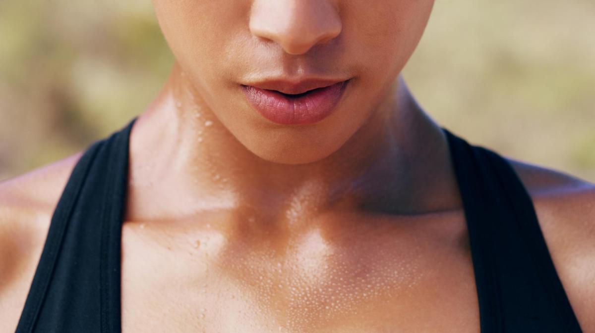 Frau mit einem Oberteil mit schwarzen Trägern schwitzt am Schlüsselbein.