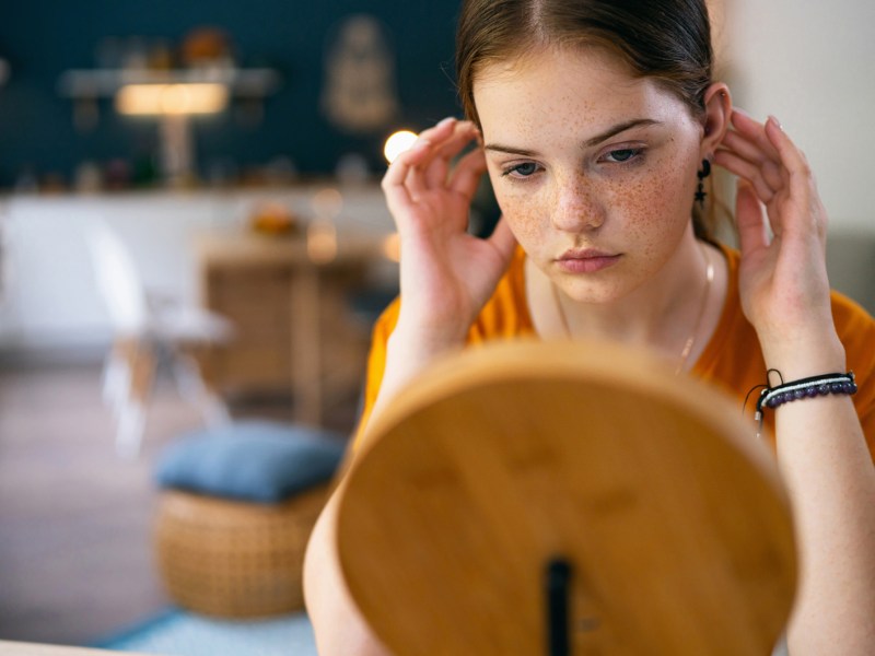 Mädchen im Teenageralter, das kritisch in den Spiegel schaut.