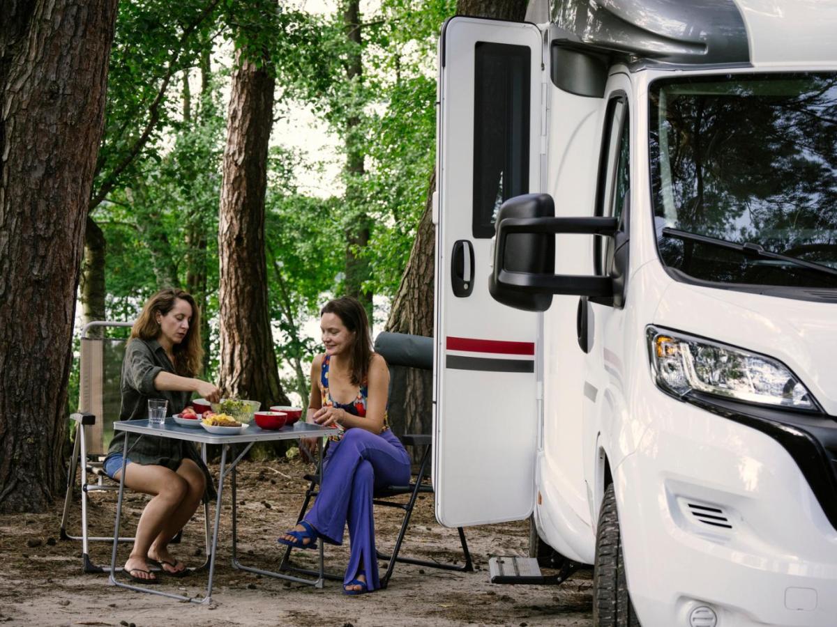 Zwei Frauen sitzen an einem Campingtisch in der Natur neben einem Wohnmobil.