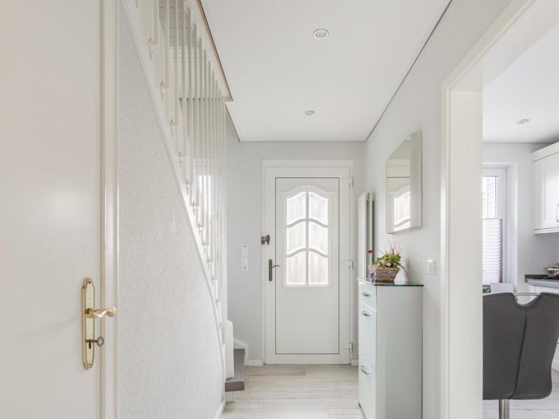 Foto eines Hausflurs mit einer weißen Haustüre und einer weißen Treppe und einem weißen Schmalen Schuhschrank.