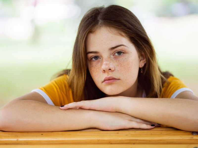 Mädchen im Teenageralter lehnt gelangweilt auf einem Tisch draußen.