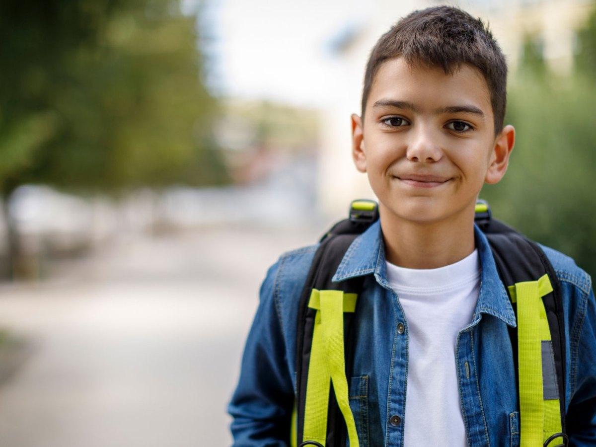 Portr&auml;t eines Jungen, ca. 10 Jahre alt, steht mit einem Rucksack auf der Stra&szlig;e und schaut freundlich in die Kamera.