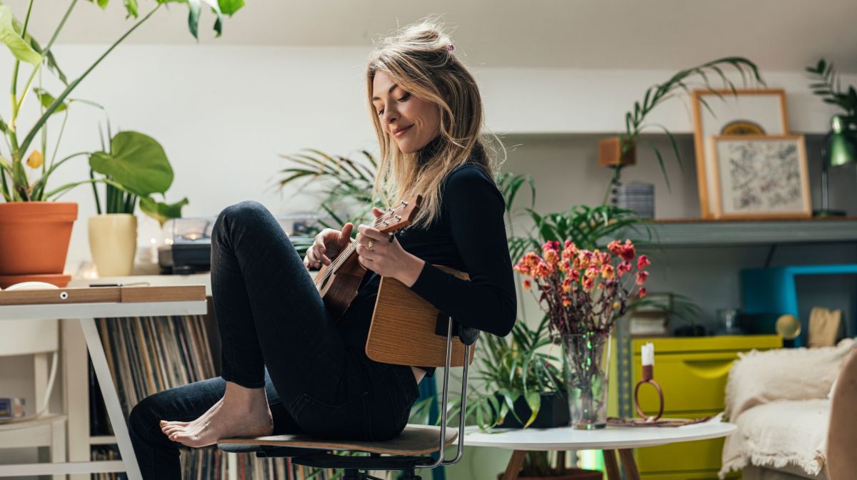 Frau spielt Ukulele in üppig dekorierter Wohnung