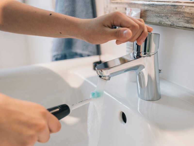 Hände mit Zahnbürste über Waschbecken im Bad