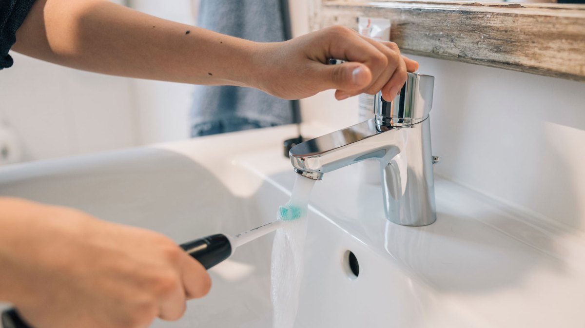 Hände mit Zahnbürste über Waschbecken im Bad