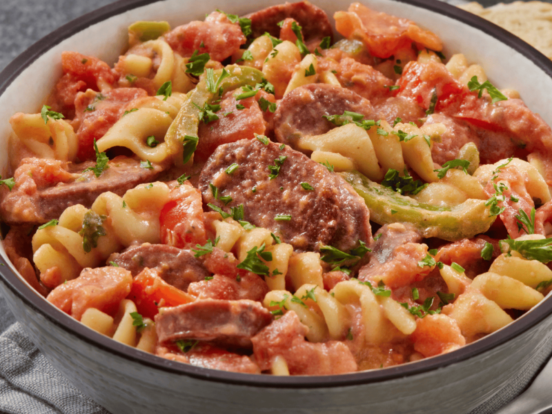 Eintopf mit Nudeln, Würstchen und Paprika in heller Schüssel.