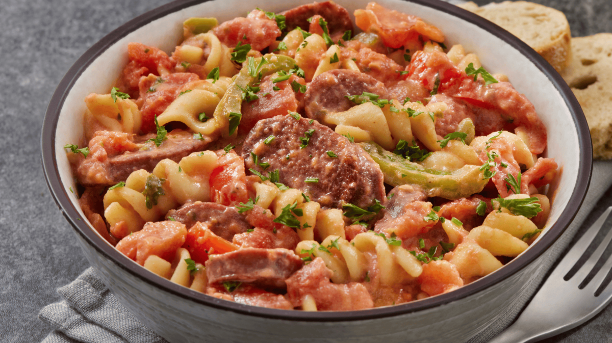 Eintopf mit Nudeln, Würstchen und Paprika in heller Schüssel.