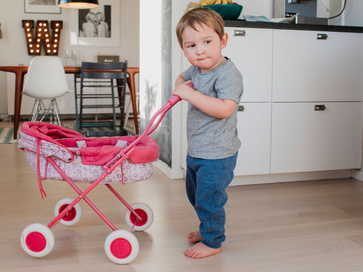 Kleiner Junge spielt mit Puppenwagen in der K&uuml;che.