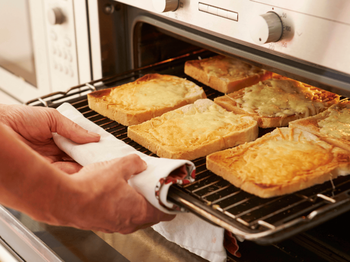 Person holt &uuml;berbackenene Toastscheiben aus Ofen.