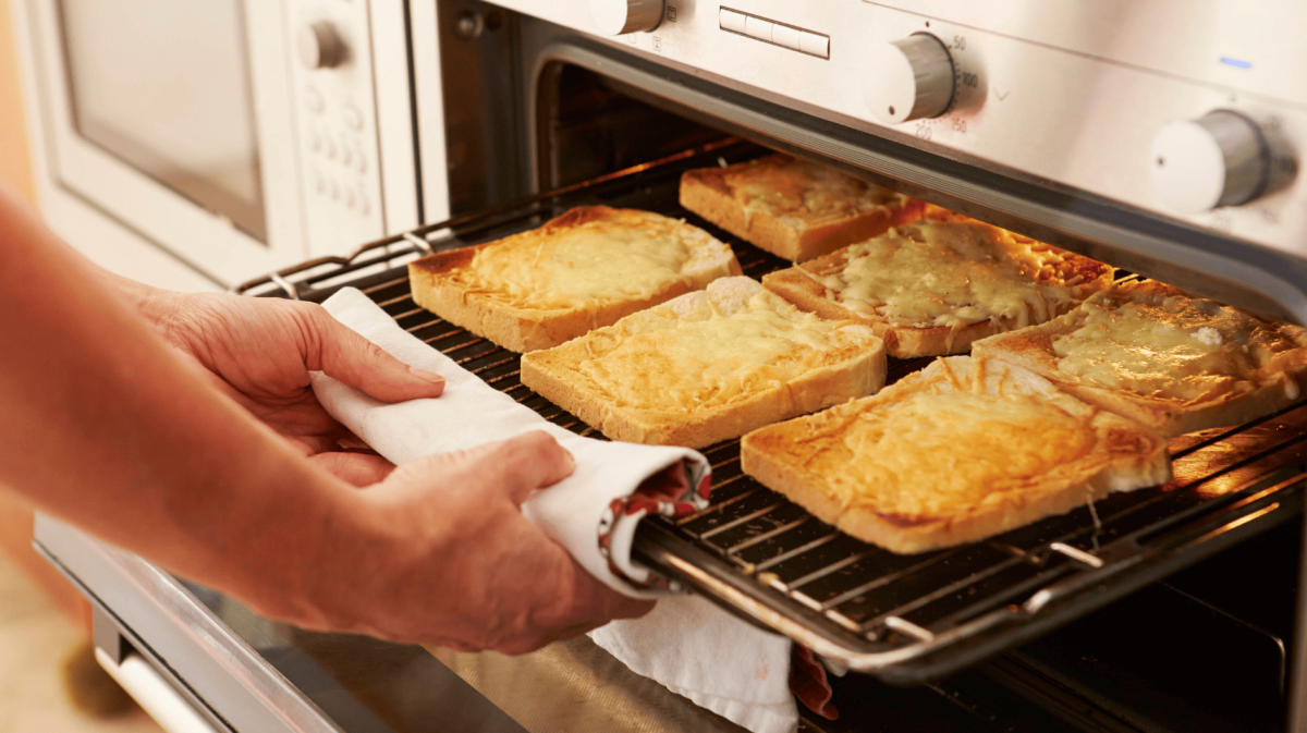 Person holt überbackenene Toastscheiben aus Ofen.