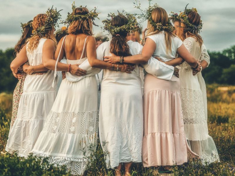 Frauen tanzen in weißen Kleidern und mit Blumenkränzen im Haar