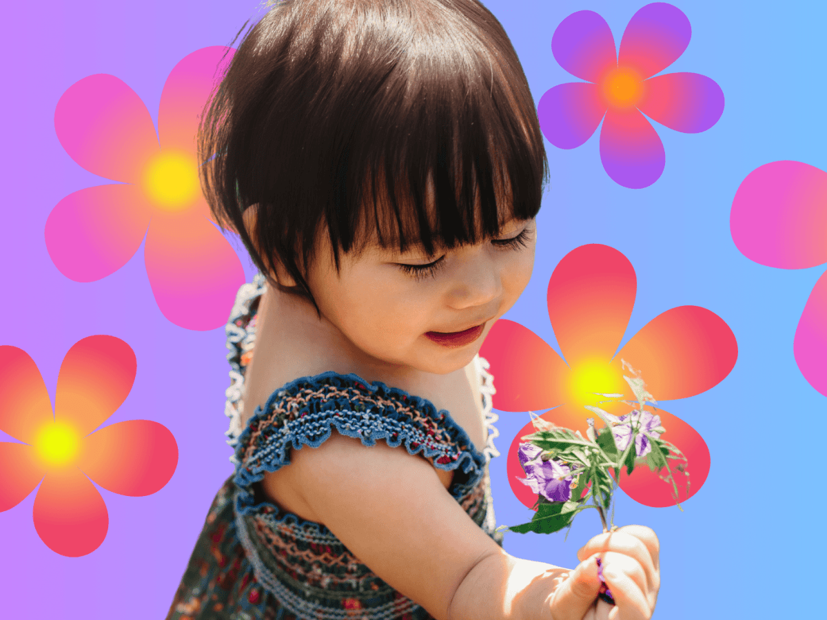 Kleinkind mit Kleid steht auf einer Wiese und h&auml;lt eine Blume in der Hand.