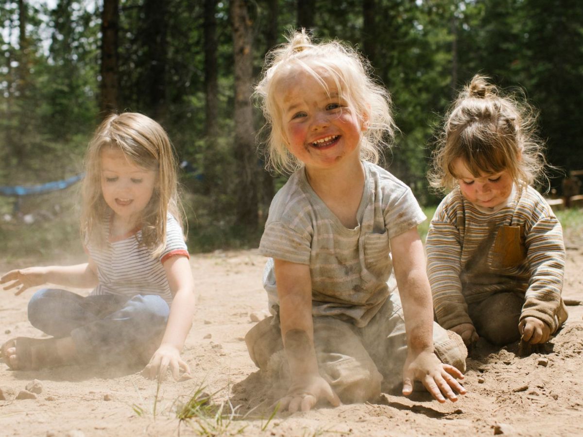 Drei fröhliche Mädchen spielen im Sand in einem Wald