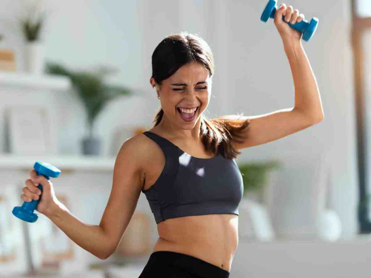Frau treibt gut gelaunt mit Hanteln Sport und tr&auml;gt einen Sport-BH.