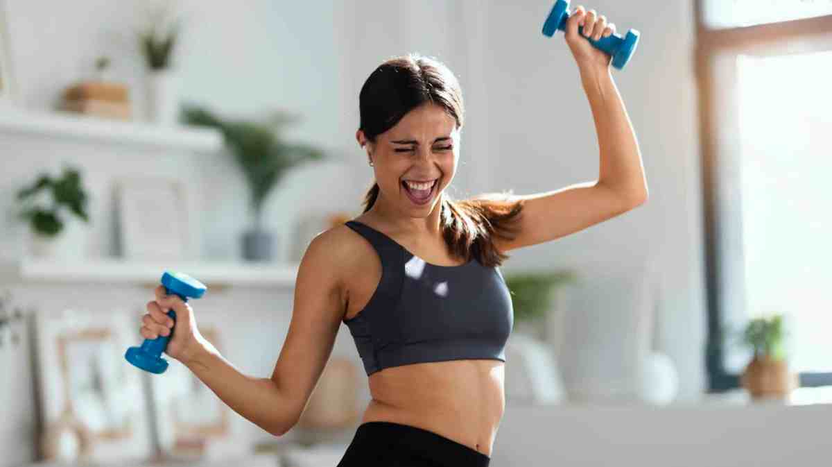 Frau treibt gut gelaunt mit Hanteln Sport und trägt einen Sport-BH.