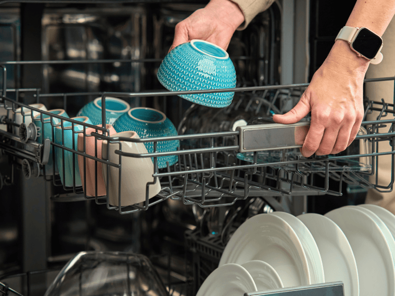 Person räumt Geschirr, eine blaue Schale, in Spülmaschine.