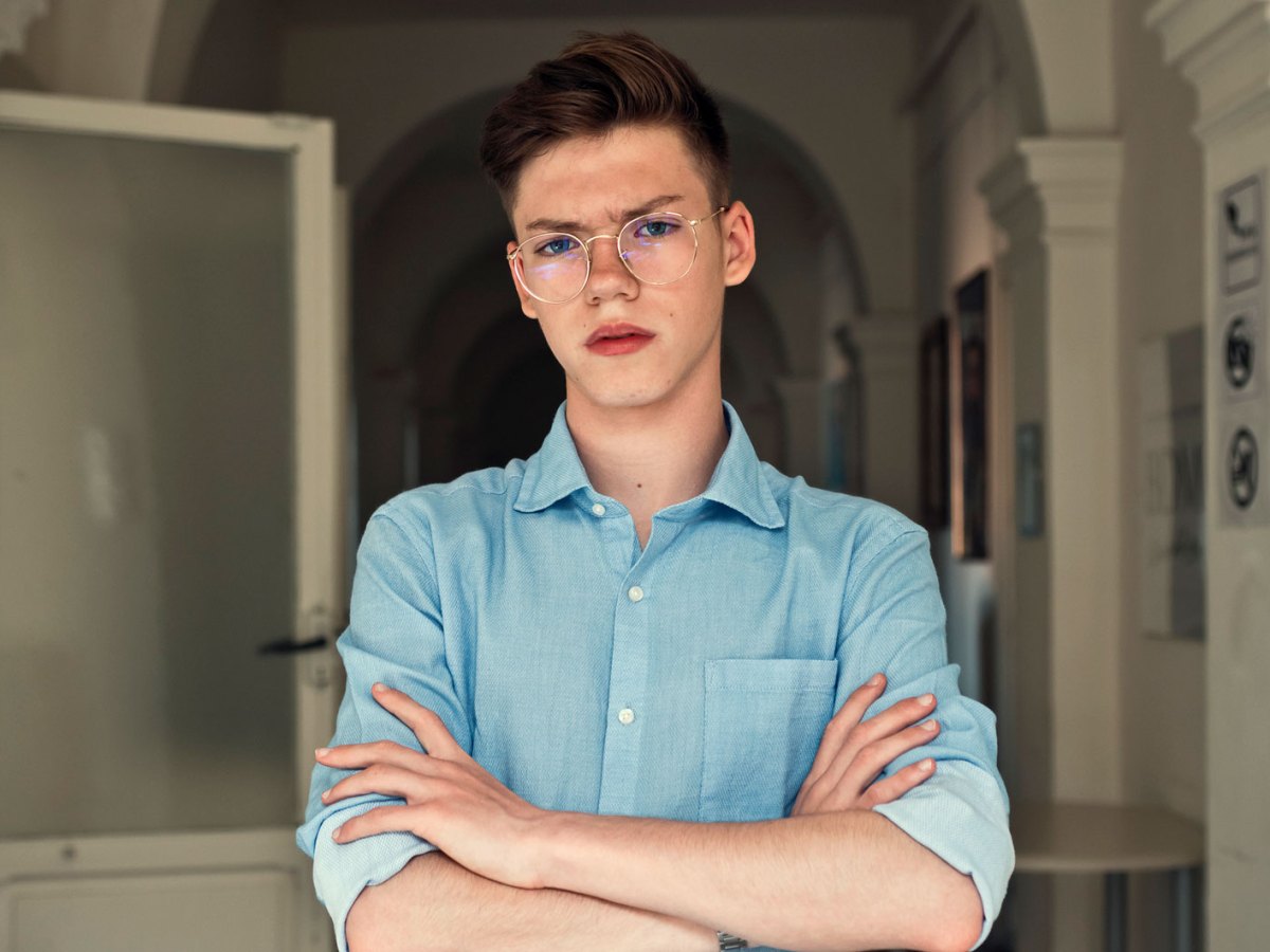 Portr&auml;t eines Teenagers, der mit verschr&auml;nkten Armen und b&ouml;se Blick im Flur einer Wohnung steht.