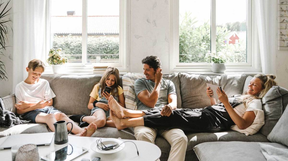 Vierköpfige Familie sitzt auf dem Sofa, alle haben ein digitales Gerät in den Händen.