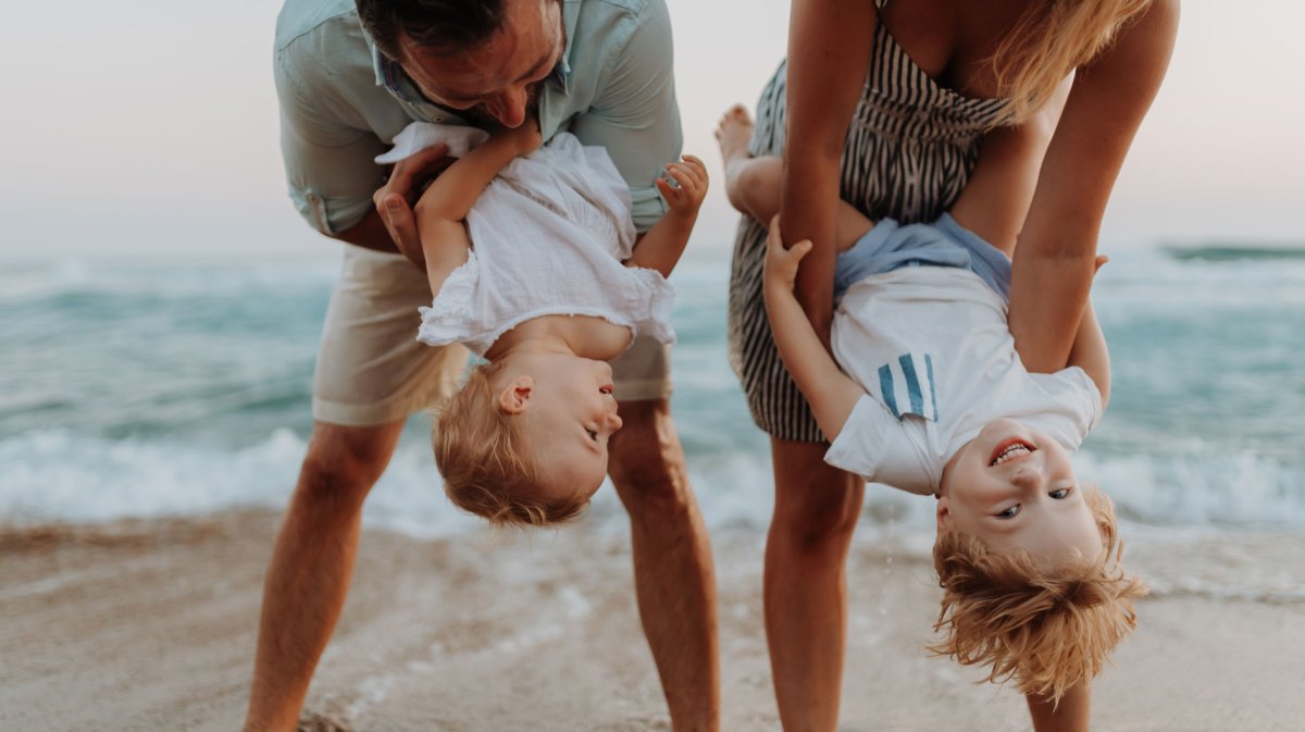 Junge Familie mit zwei kleinen Kindern, die gemeinsam am Strand herumalbern.
