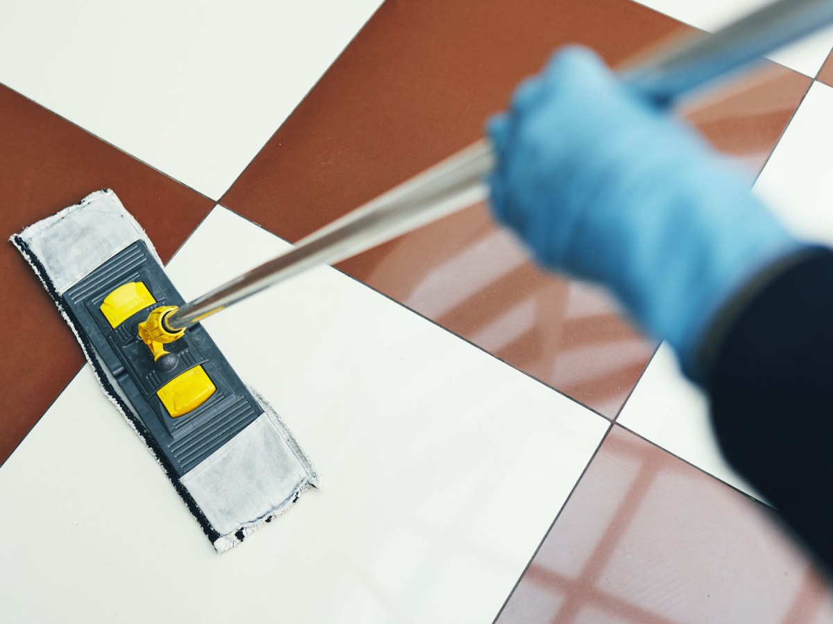 Eine Hand hält einen Mopp und wischt braun weiß karierte Fliesen.