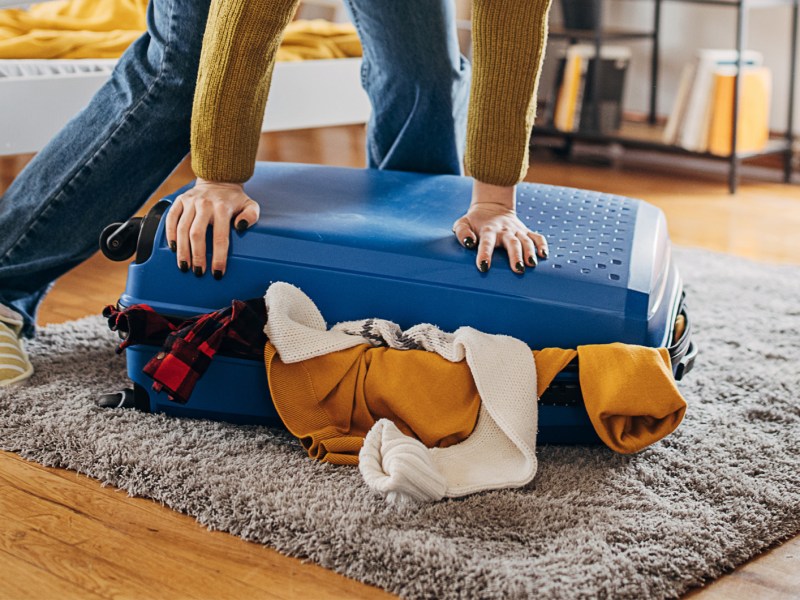 Frau, die versucht ihren vollen Koffer zu schließen.