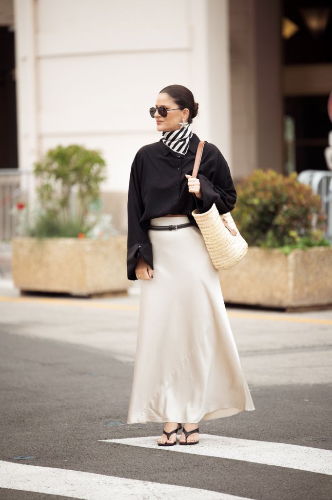 Frau mit schwarzer Bluse und hellem Rock und dazu ein schwarz-weißes Tuch um den Hals.