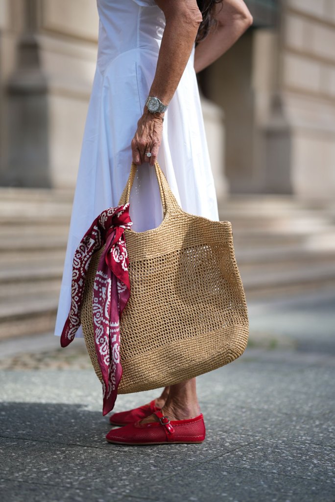 Frau mit weißem Kleid und Bast-Tasche an der ein rotes Bandana befestigt ist.