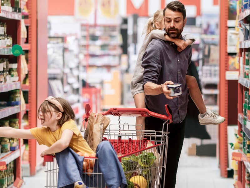 Vater steht mit seinen beiden Töchtern im Gang eines Supermarkts.