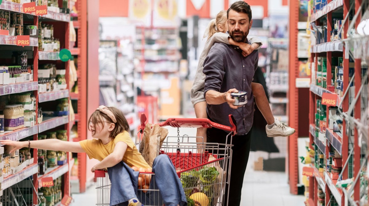Vater steht mit seinen beiden Töchtern im Gang eines Supermarkts.