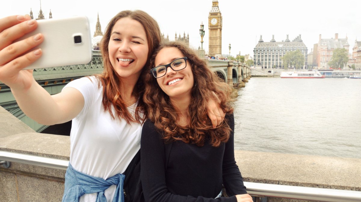 Zwei Teenager-Mädchen stehen in London an der Themse und machen ein Selfie mit Big Ben im Hintergrund.