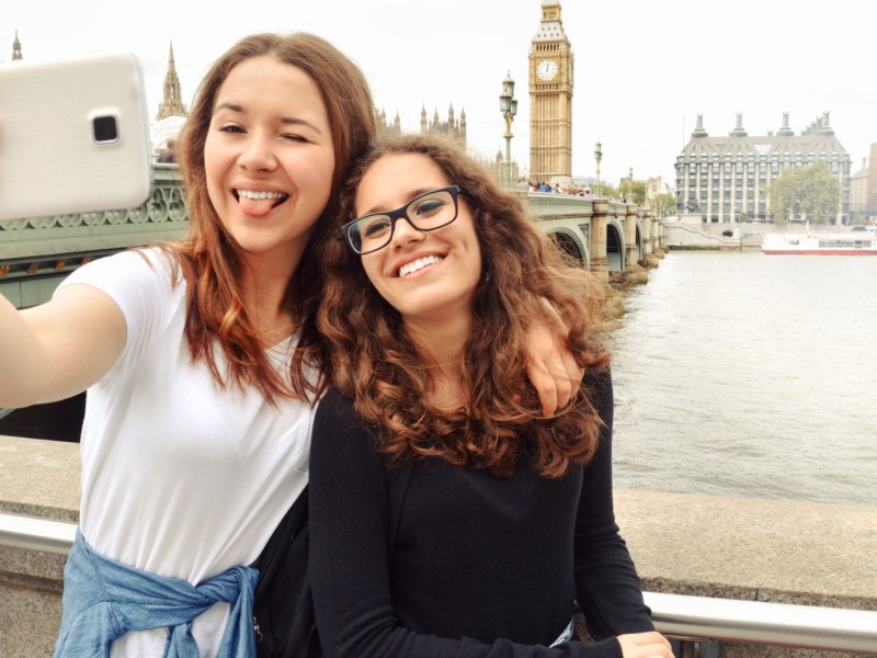 Zwei Teenager-Mädchen stehen in London an der Themse und machen ein Selfie mit Big Ben im Hintergrund.