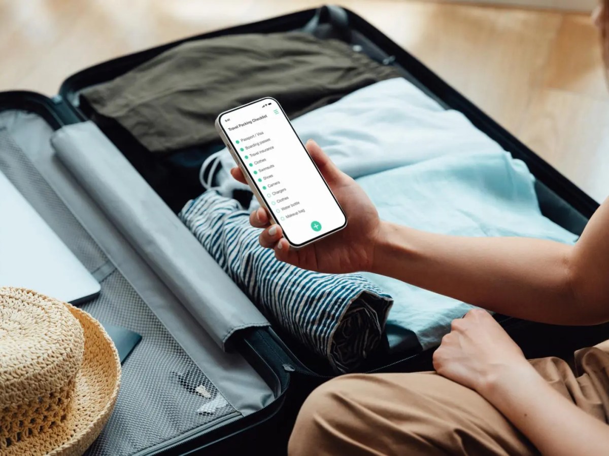 Frau packt Koffer mit einer Packliste auf ihrem Smartphone.