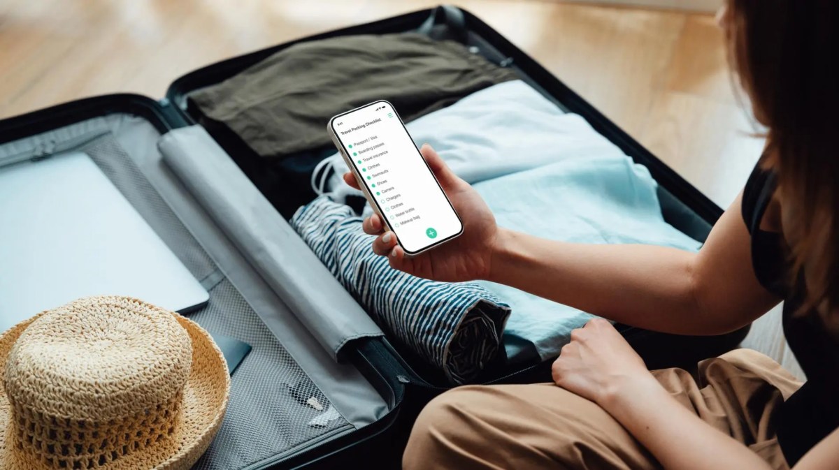 Frau packt Koffer mit einer Packliste auf ihrem Smartphone.