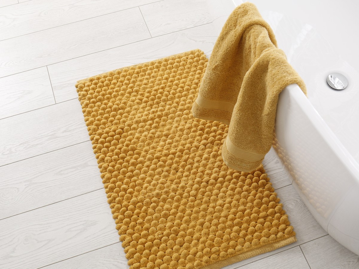 Gelbe Badematte liegt vor Badewanne