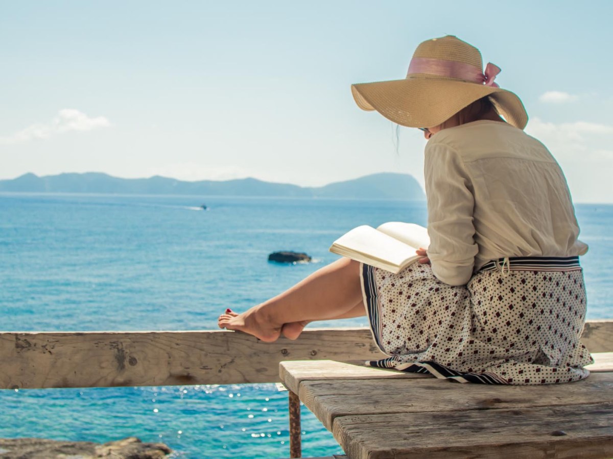 Junge Frau liest ein Buch auf einer Holzterrasse vor dem Meer