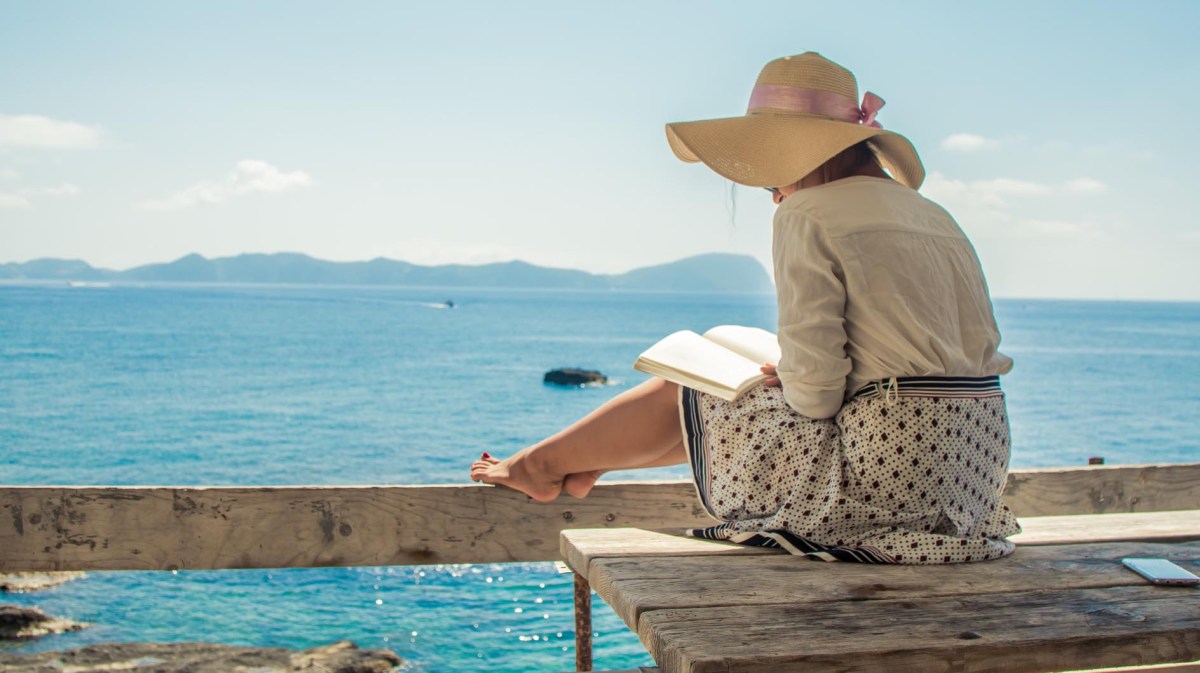 Junge Frau liest ein Buch auf einer Holzterrasse vor dem Meer