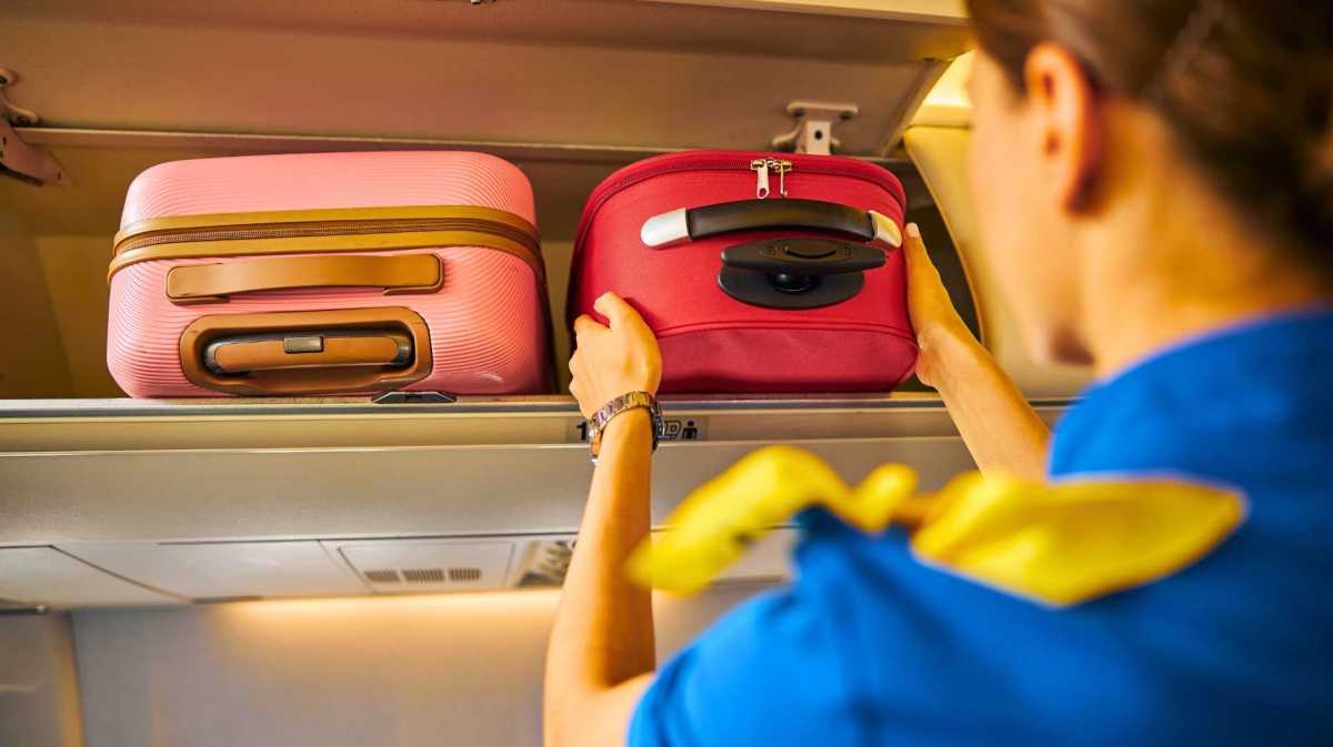 Flugbegleiterin lagert Handgepäck im Flugzeug.