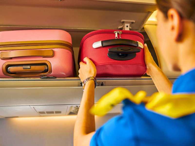 Flugbegleiterin lagert Handgepäck im Flugzeug.