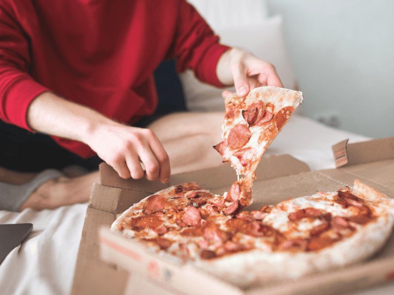 Person isst Pizza auf Bett.