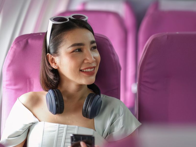 Junge Frau mit Kopfhörern sitzt auf lila Sitzen im Flugzeug
