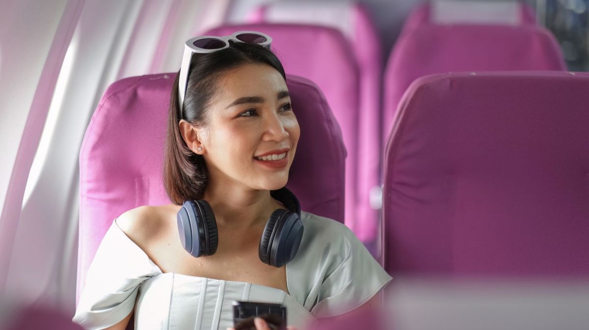 Junge Frau mit Kopfhörern sitzt auf lila Sitzen im Flugzeug