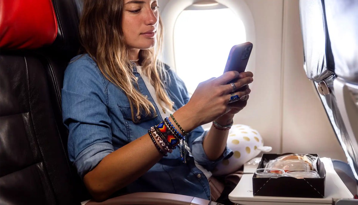 Frau sitzt im Flugzeug mit Essen vor sich und hat Handy in der Hand