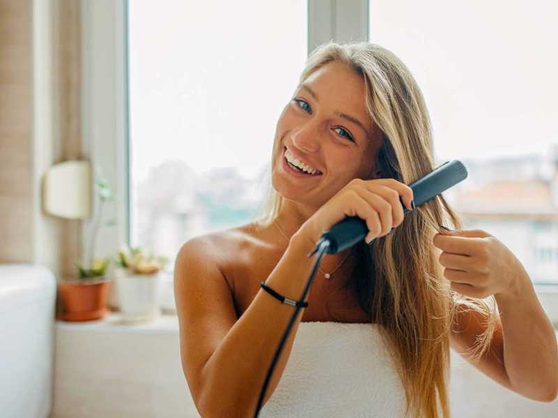 Junge Frau glättet sich die Haare.